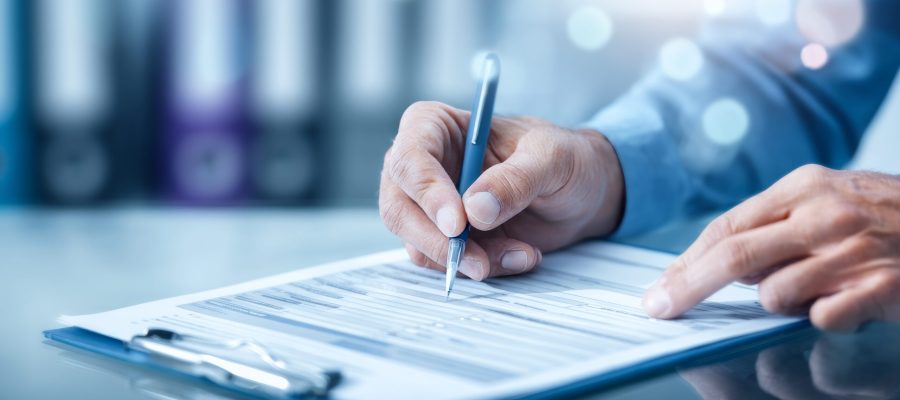 Closeup image of hands filling out patient intake forms while sitting at a table, conveying the administrative aspect of healthcare services and documentation.