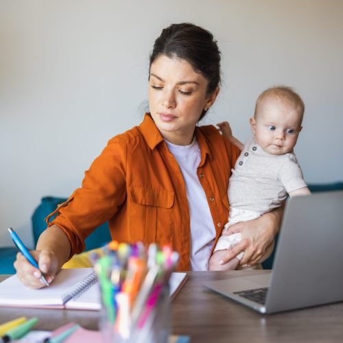 Busy mother writing in notes while babysitting her daughter and working at home.