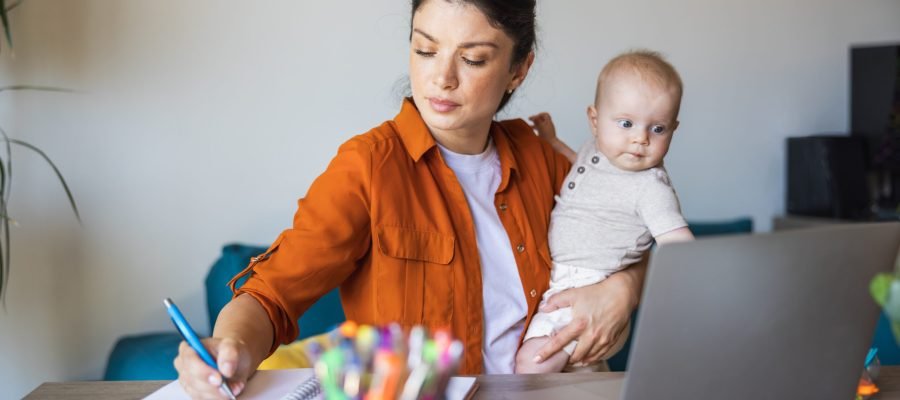 Busy mother writing in notes while babysitting her daughter and working at home.
